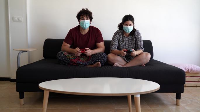 一对夫妇戴着口罩，坐在沙发上打游戏