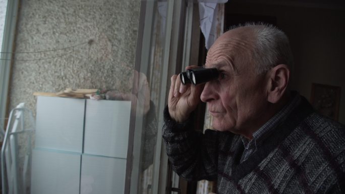 老人拿着黑色双筒望远镜透过窗户看