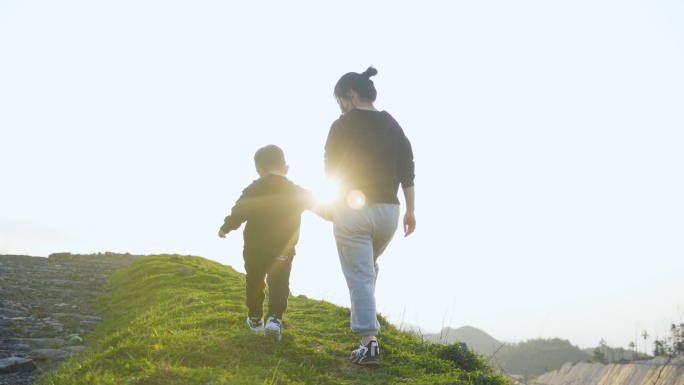 年轻妈妈牵着小孩山顶行走逆光剪影温馨母爱