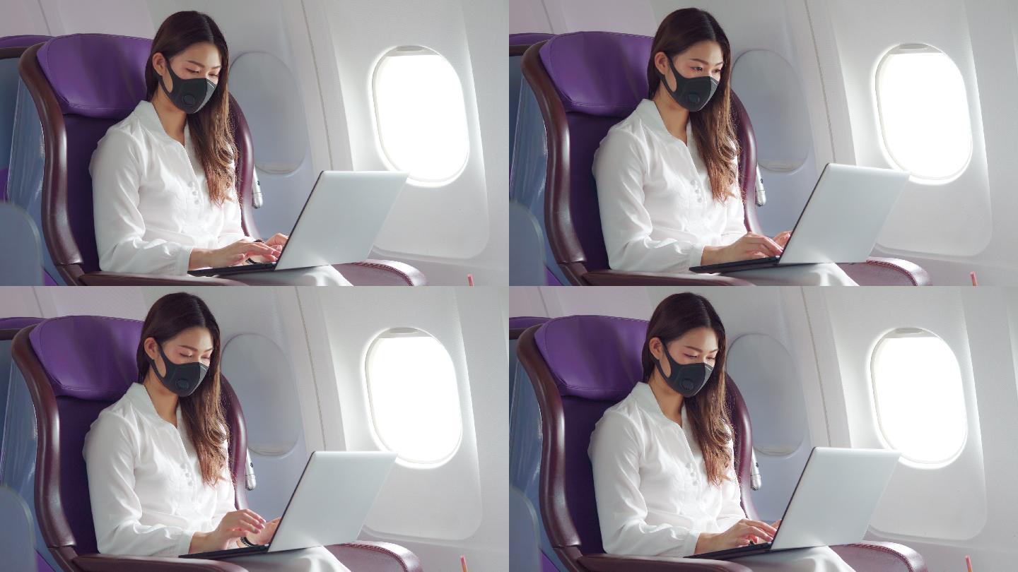 年轻女子戴着口罩使用笔记本电脑坐在飞机上