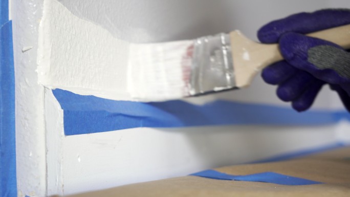 带手套的油漆工手用刷子刷墙壁边缘。