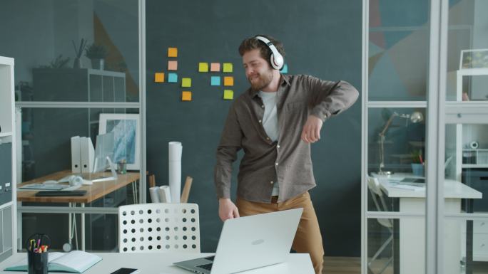 快乐的年轻人戴着耳机在工作场所跳舞