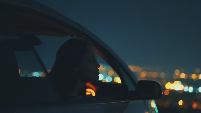 年轻女子坐在车里灯光璀璨车内女人窗外风景