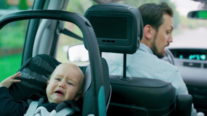 哭泣的男婴坐在车内后排座椅上