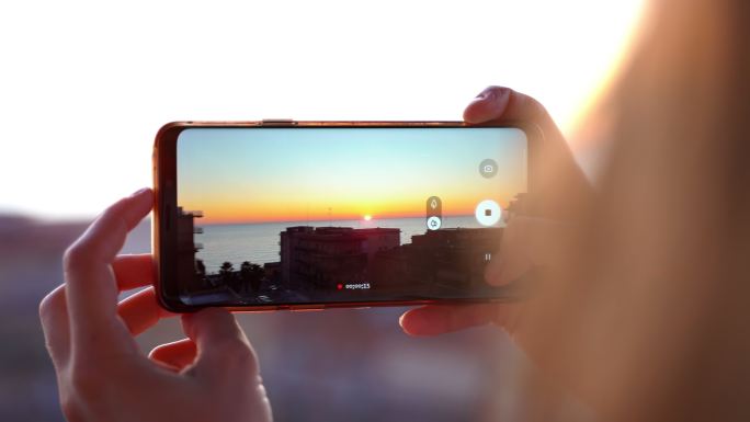 女性手持智能手机在海上拍摄日落