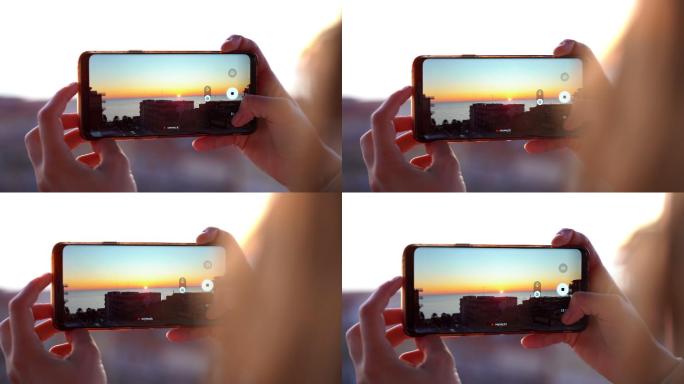 女性手持智能手机在海上拍摄日落