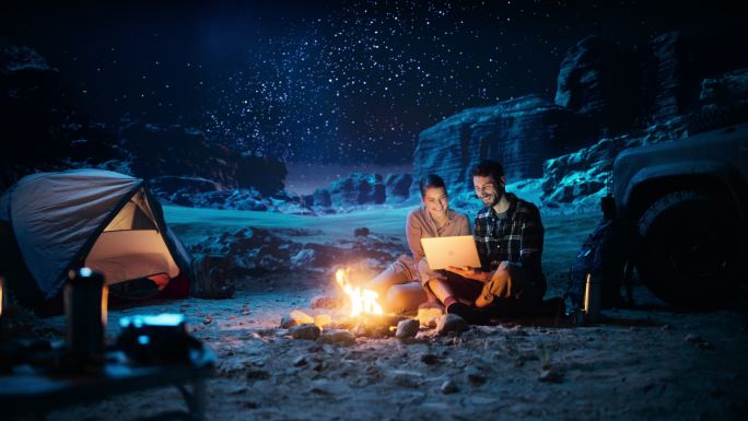 幸福的夫妇晚上在峡谷露营，使用笔记本电脑