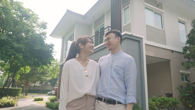 年轻夫妇站在新房子前微笑