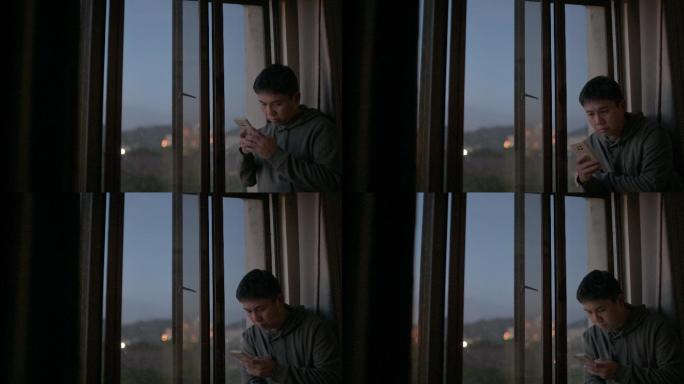 日落时分，男子从在窗户旁使用智能手机