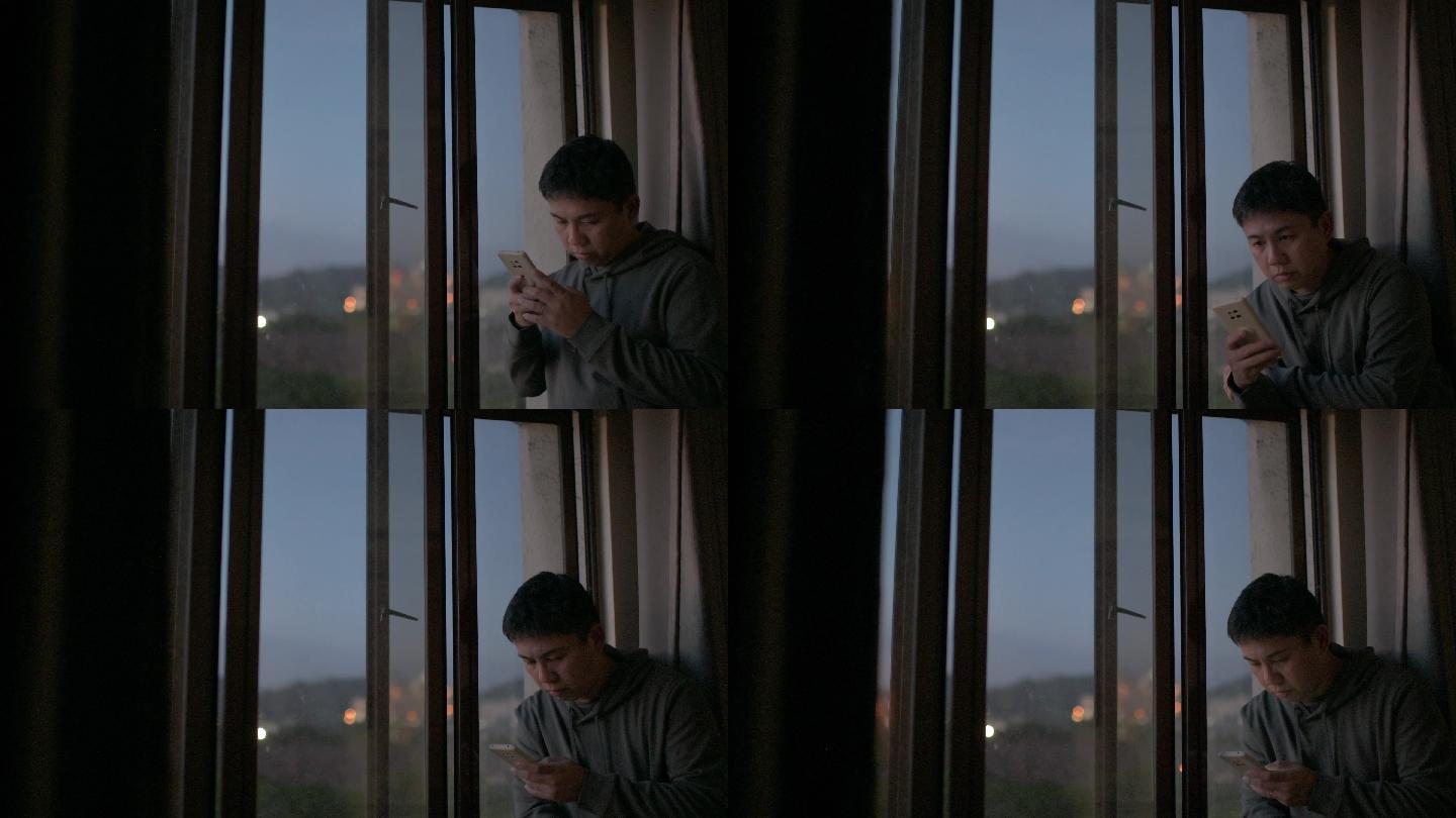 日落时分，男子从在窗户旁使用智能手机