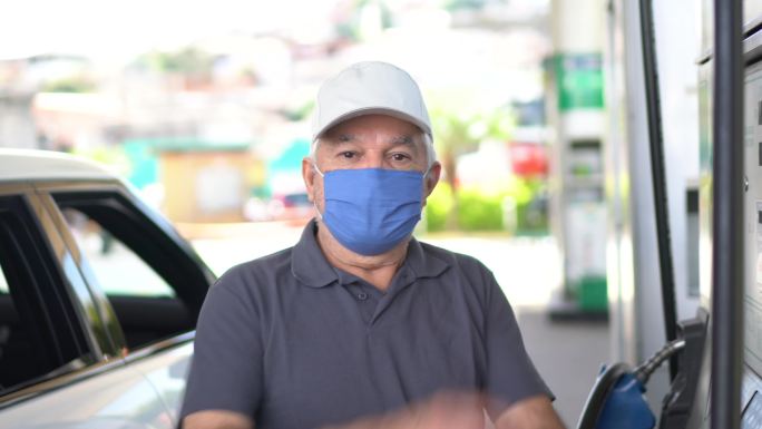 一位戴着口罩的老人在加油站给汽车加油