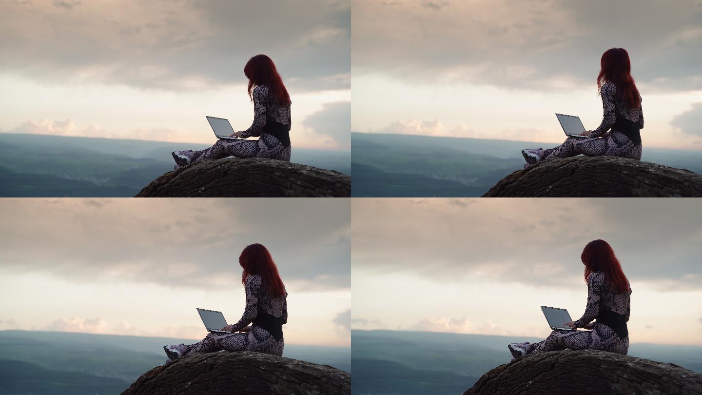 女博主旅行者坐在山顶上用笔记本电脑打字