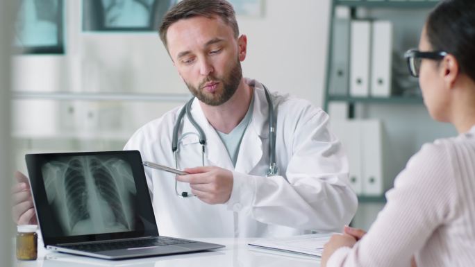 男医生在笔记本电脑上向女性展示肺部X光片