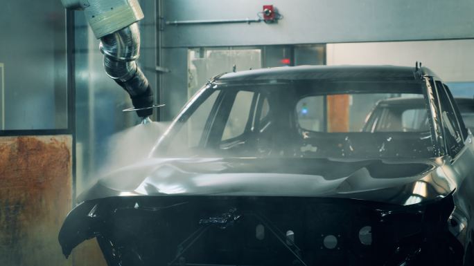 在一家汽车制造厂，机械臂在车身上喷漆