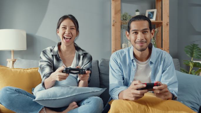 年轻夫妇坐在沙发上玩电子游戏