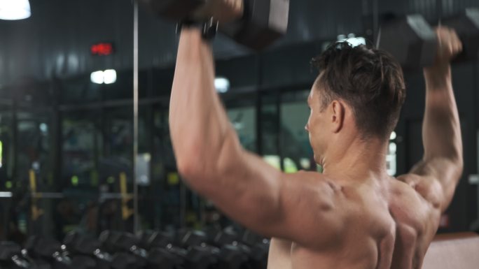 健美运动员在健身房用哑铃锻炼肩膀。