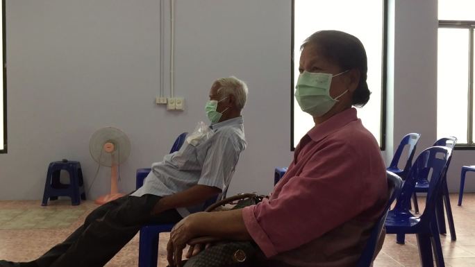 戴着外科口罩的老人坐在医院空荡荡的候诊室
