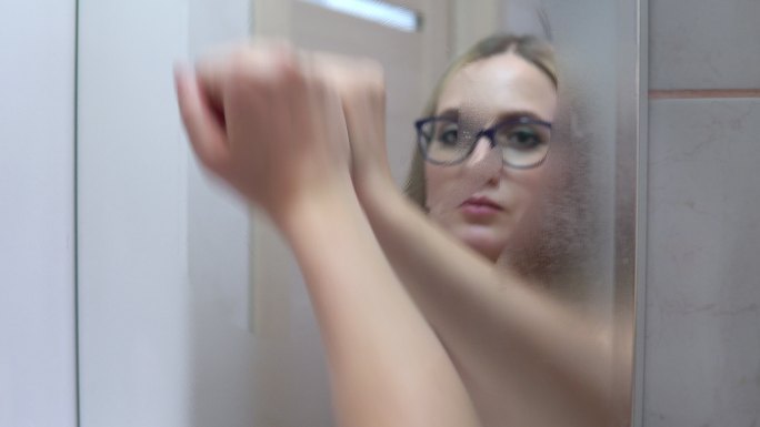 浴室里的女人用手擦拭着雾气弥漫的镜子