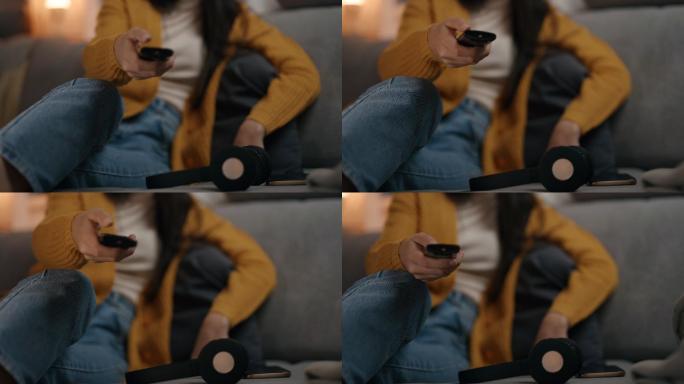 一个女人坐在家里的沙发上用遥控器切换频道