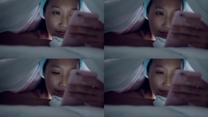 年轻女性晚上在床上玩手机。