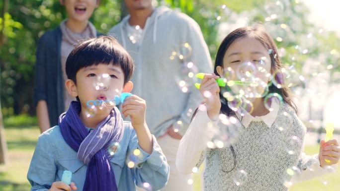 小女孩和男孩在公园吹泡泡，父母在后面看着