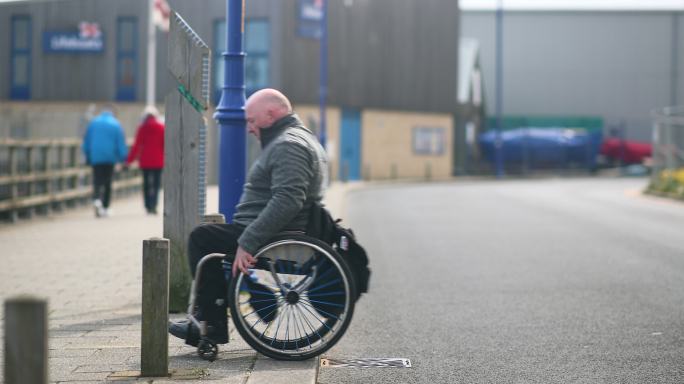 一名残疾男子坐着轮椅在过马路。