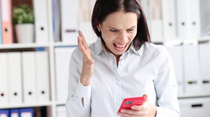 愤怒的女人看着手机屏幕，在办公室里大喊
