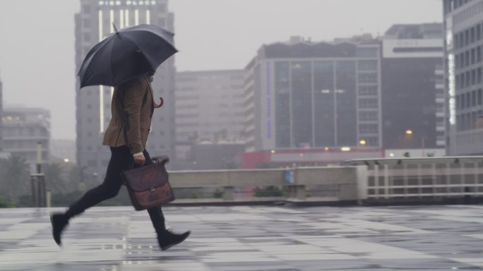 商人撑着雨伞，在城市户外雨中奔跑