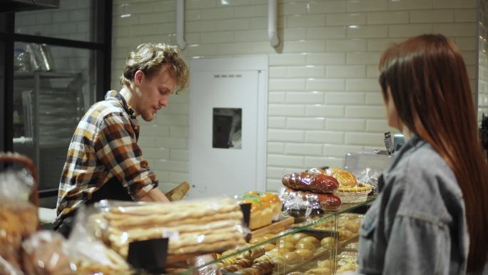 卖面包的人在商店里为女顾客包装法式面包