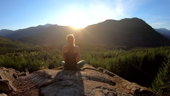 阳光下冥想的女人岩石上青山夕阳瑜伽户外