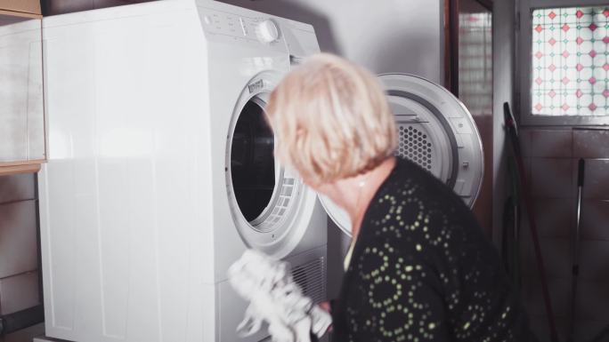 年长的女士正在将洗衣机清洗一批衣物。