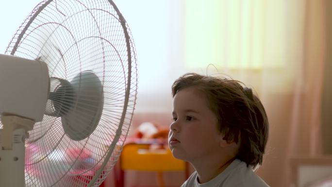 孩子在家里享受着电扇带来的凉风。