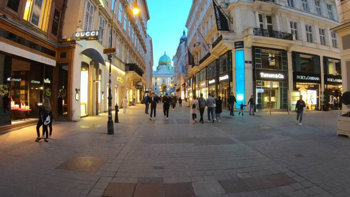 游客和居民在晚上沿着维也纳的街道散步。