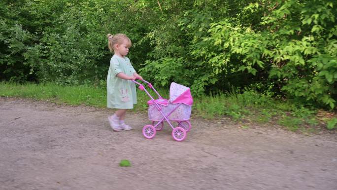 带着婴儿车玩具在夏季公园散步的小女孩