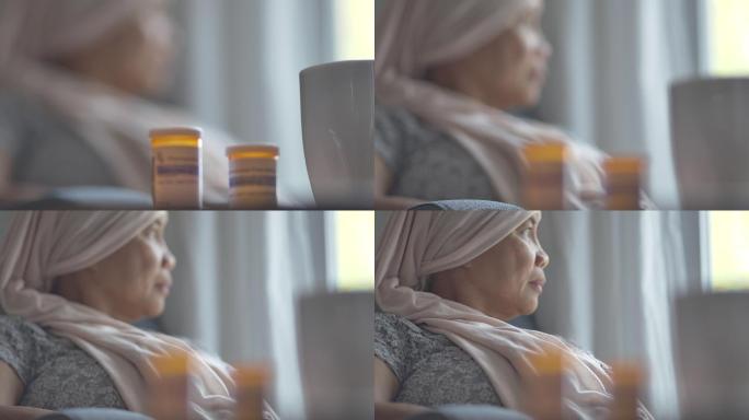 一位身患癌症的老年妇女戴着头巾坐在家中