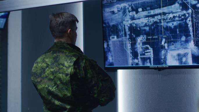 军官在墙上的电视屏幕上观看卫星监控录像