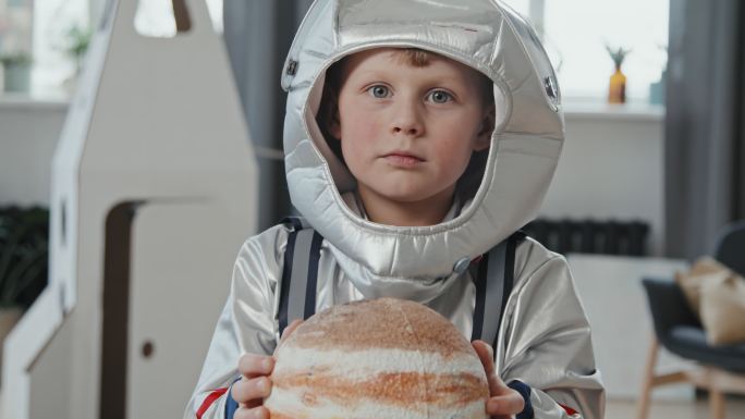 穿着太空服的可爱男孩拿着行星模型
