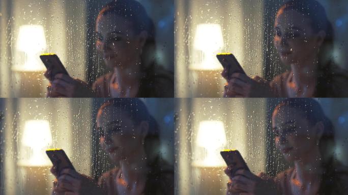 使用手机的女人下雨的窗户雨滴滑落女人发信
