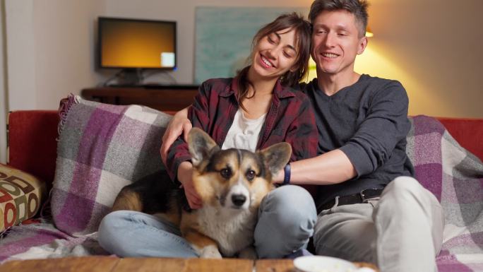 一对夫妇和可爱的宠物科基犬坐在沙发上