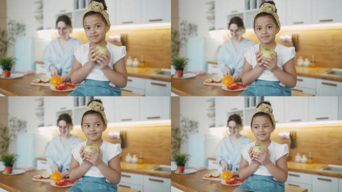 小女孩坐在厨房的桌子上，手里拿着青苹果
