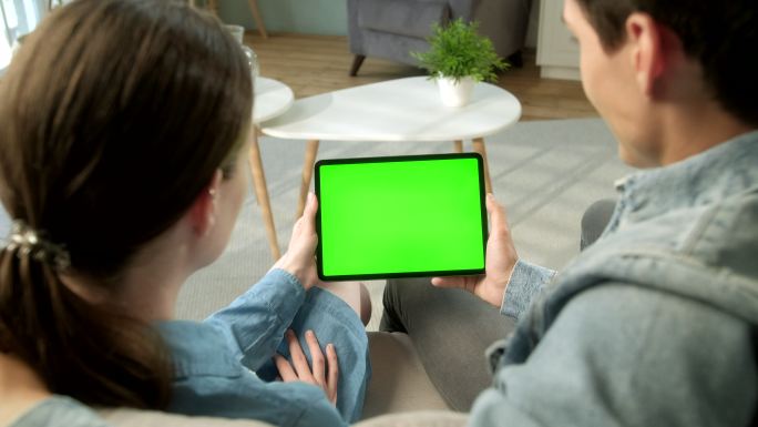 在家坐在沙发上用绿色屏幕电脑的年轻夫妇