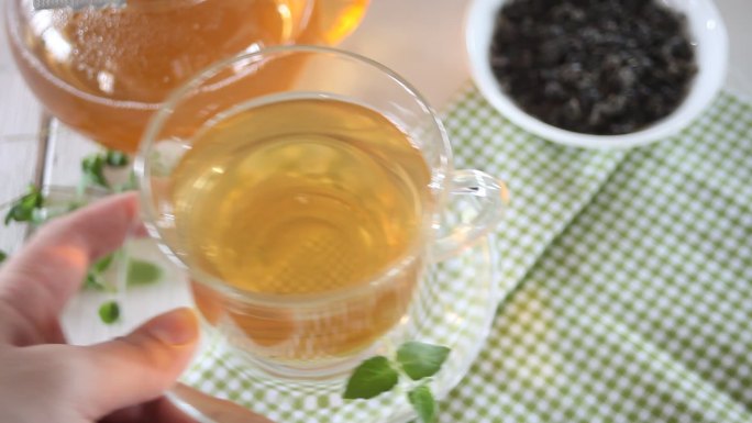 女士将一杯新鲜的绿茶或红茶和薄荷放在桌上