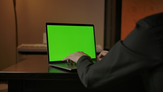 男子在绿色屏幕的笔记本电脑键盘上打字