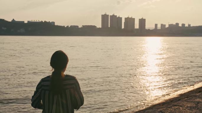 女子迎着夕阳在江边拍照