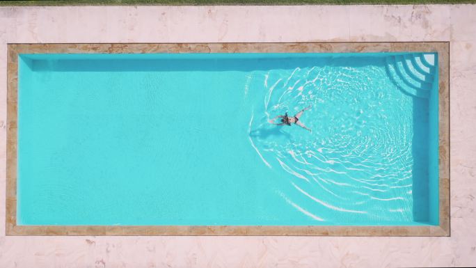 一名女子在私人别墅泳池游泳的鸟瞰图