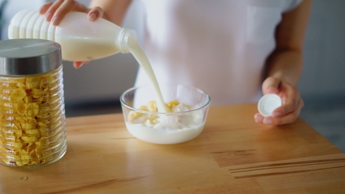 女人用手把牛奶倒进装有玉米片的玻璃碗里