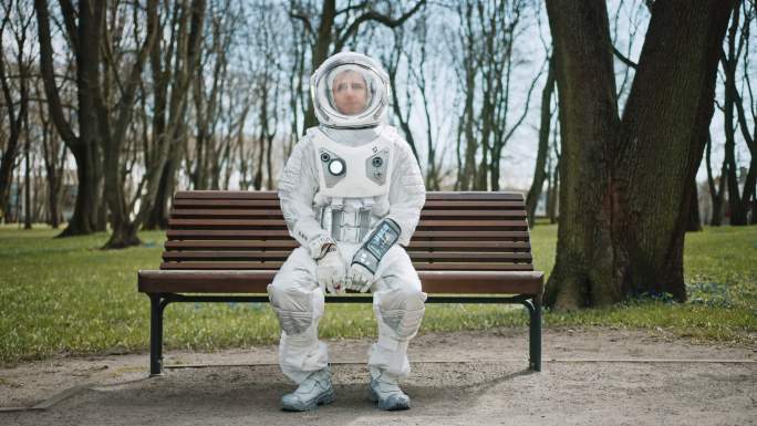 穿着太空服的悲伤男子坐在公园的长椅上。