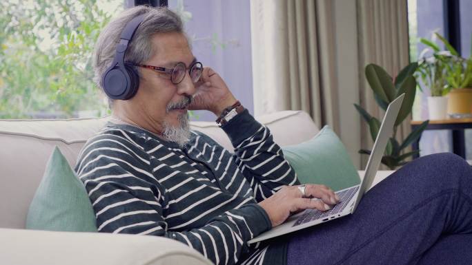 男性坐在客厅的沙发上，戴着耳机听音乐