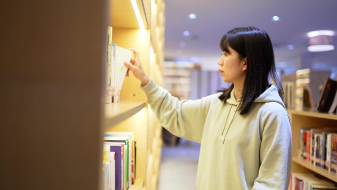 年轻女子图书馆书架前边走边查找书本