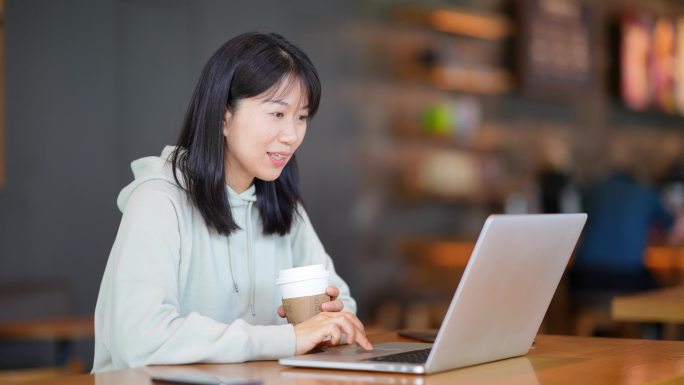 年轻女子在咖啡店使用笔记本电脑视频通话